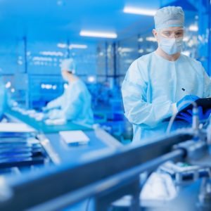 Pharmaceutical factory worker operating production line at pharmacy industry, man use clipboard for control quality. Blue light toning, manufacturing surgery kit box Pharmaceutical factory worker operating production line at pharmacy industry, man use clipboard for control quality. Blue light toning, manufacturing surgery kit box.
